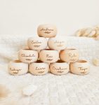 Argola Marcador de Lugar Personalizada | Casamento e Batizado - PIPÁPÁ - Amor em Madeira Pyramid of smooth wooden name blocks, each with a handwritten name (Andrea, Carlos, Angie, Elisabethe, Rui, Rita, Rodrigo, Laura, Cristiana, Tiago) and a small leaf engraving on a light background.
