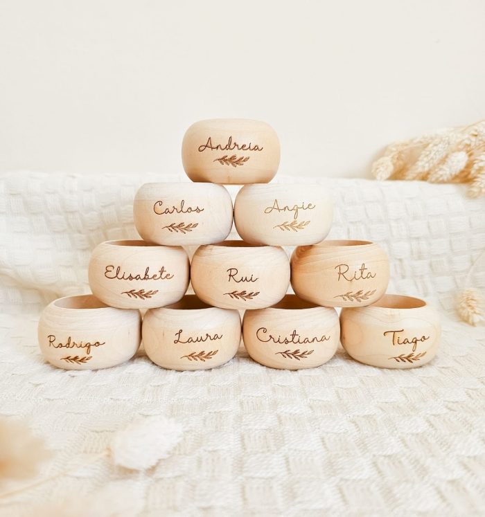 Pyramid of smooth wooden name blocks, each with a handwritten name (Andrea, Carlos, Angie, Elisabethe, Rui, Rita, Rodrigo, Laura, Cristiana, Tiago) and a small leaf engraving on a light background.
