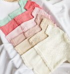 conjunto-malha-verao-bebe - PIPÁPÁ - Amor em Madeira Stack of pastel knit baby sweaters with lace edges on a white textured blanket surface.
